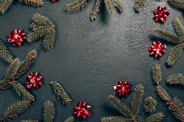 Minimal Christmas border composition with fir branch and red bows on dark background, flat lay, top view.