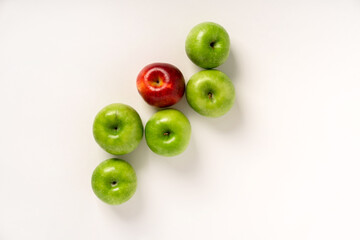 Green apples and one red one are laid out on a white table