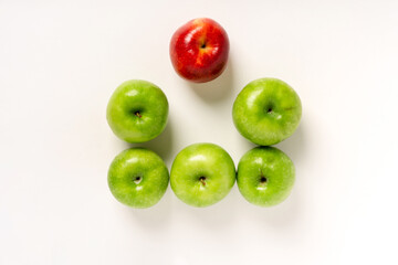 Green apples and one red one are laid out on a white table