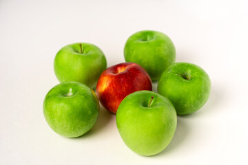 Green apples and one red one are laid out on a white table