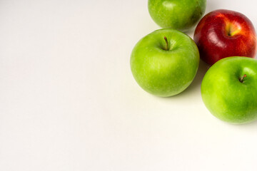 Green apples and one red one are laid out on a white table