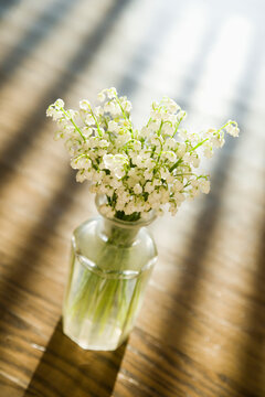 Lily of the valley flowers in glass vase on wooden table.