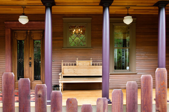 Wooden Fence And House Porch With Columns And Bench.