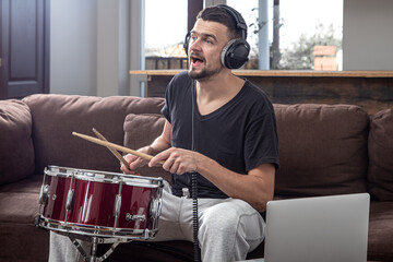 A young man with headphones learns to play the drum using online lessons.