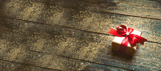 Christmas background - gift box with red bow on wooden board with festive golden glitter
