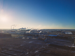 Factories, pipes with smoke on a Sunny snowless winter day against a blue sky, photo from a drone. Concept of ecology and nature protection.