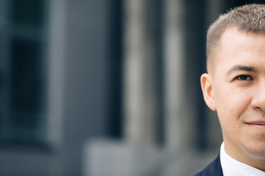 Close up of half face of upset Caucasian young businessman in looking straight to camera while standing outdoors near modern office building
