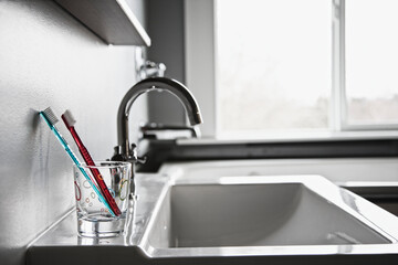 Toothbrushes in drinking glass in domestic bathroom.