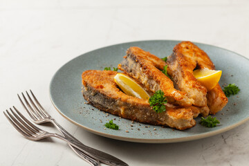 Fried carp in pieces, served on a gray plate. Marbled bright background.