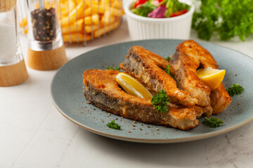 Fried carp in pieces, served on a gray plate. Marbled bright background.