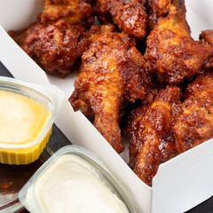 Takeaway box of crispy grilled chicken legs with a spicy marinade served with a hot chili dipping sauce, close up view