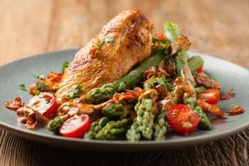 Roasted chicken breast, served on asparagus with tomato sauce, dried tomatoes. Front view.