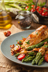 Roasted chicken breast, served on asparagus with tomato sauce, dried tomatoes. Front view.