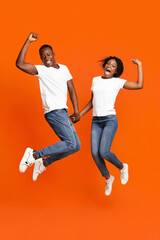 Fototapeta na wymiar Emotional black couple holding hands and jumping up