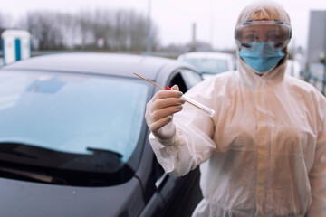 Medical heath care worker in protective white suit with gloves standing at checkpoint and holding test kit for covid-19.