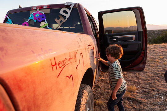 young boy writing on paint on an old pickup truck