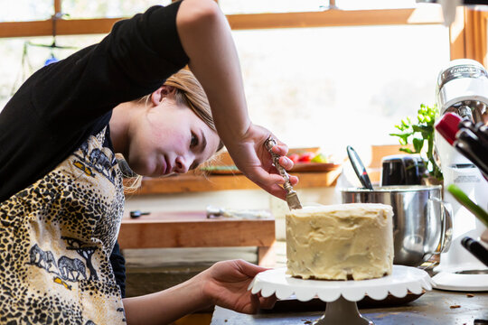 Teenage girl in kitchen applying icing to cake 