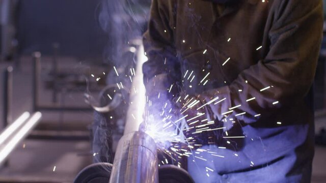 Worker welding metal pipe in big factory