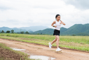 Happy Funny little asian girl fitness woman running at morning tropical forest trail. Athletic young child running in the nature. Healthy lifestyle.