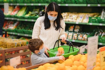 Mom and son wearing protective masks choose fruits to buy in the store