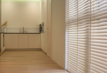 Wood blinds in the interior, in the kitchen. Motorized venetian wooden blinds beige color on large windows. Slats 50mm wide. Wood floor, beige walls.