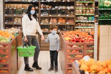 Young woman and her kid wearing protective face masks shop a food at a supermarket during the coronavirus epidemic or flu outbreak