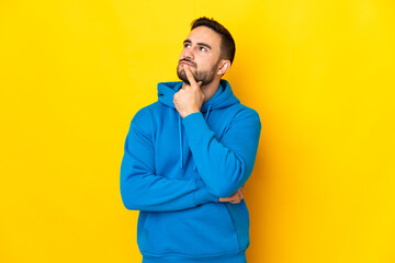 Fototapeta premium Young caucasian handsome man isolated on yellow background having doubts while looking up