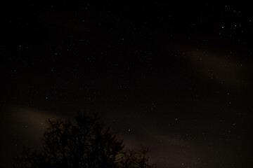 View of stars in a clear night sky with motion in clouds moving acroos the sky above