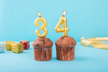 34 Number gold candle on a cupcake against a pastel blue background thirty fourth year celebration