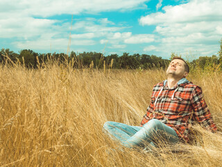 Young man relaxes sitting in nature in the grass in autumn.