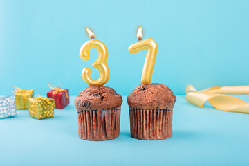 37 Number gold candle on a cupcake against a pastel blue background thirty seventh year celebration