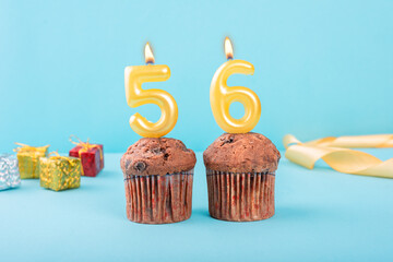 56 Number gold candle on a cupcake against a pastel blue background fifty sixth year celebration