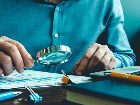The auditor checks the accounting records and reports with a magnifying glass.