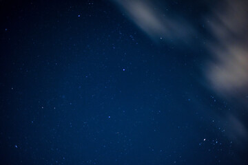 View of stars in a clear night sky with motion in clouds moving acroos the sky above
