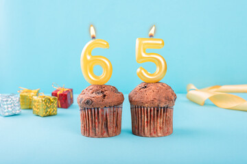 65 Number gold candle on a cupcake against a pastel blue background sixty five year celebration