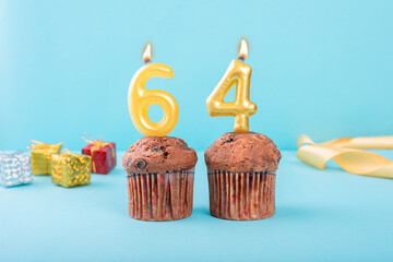 64 Number gold candle on a cupcake against a pastel blue background sixty four year celebration