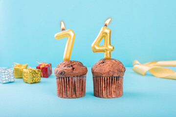 74 Number gold candle on a cupcake against a pastel blue background seventy four year celebration