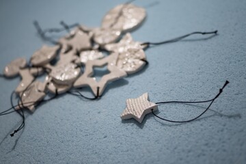 Small ornament pendant star shape figures, made of self drying white clay and shining glitter. Shallow depth of focus, bokeh effect on blue background. Christmas and New year decoration, jewel gift.