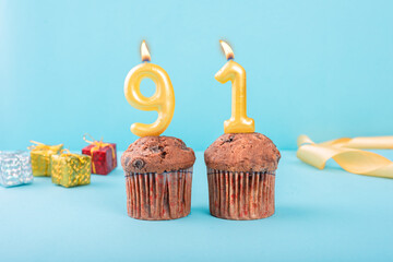 91 Number gold candle on a cupcake against a pastel blue background ninety one year celebration