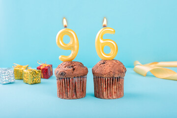 96 Number gold candle on a cupcake against a pastel blue background ninety six year celebration