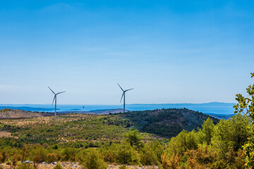 Wind turbines in Dalmatia, Croatia on landscape overgrown with bush and pine near the Adriatic sea.