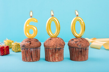 600 Number gold candle on a cupcake against a pastel blue background six hundred year celebration