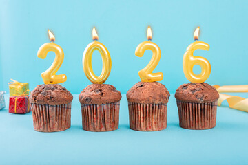 2026 Number gold candle on a cupcake against a pastel blue background two thousand and twenty six...