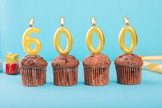 6000 Number gold candle on a cupcake against a pastel blue background six thousand year celebration