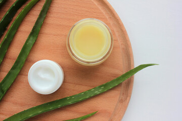 Aloe vera cream and plant on wooden background. Flat lay composition with homemade cream in glass jar and ingredient. Copy space. 