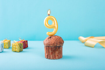 9 Number gold candle on a cupcake against a pastel blue background nine year celebration