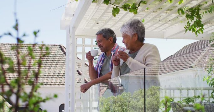 Senior mixed race couple drinking coffee on balcony in garden