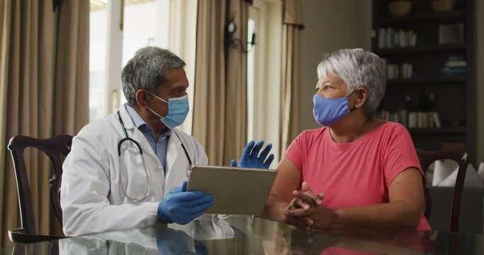 Male doctor visiting senior mixed race woman, consultation using tablet