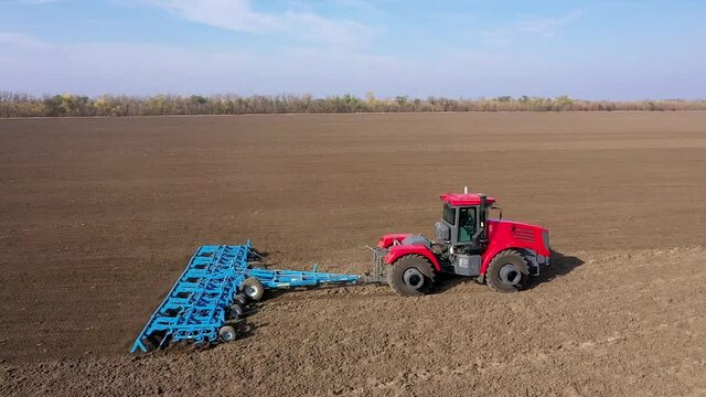 Agricultural Industry. A Red Tractor Prepares the Soil for Sowing with a Blue Cultivator