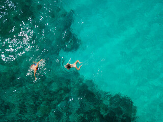 Man and woman enjoy a tropical vacation, swimming, diving, snorkeling together. Birds eye view from high above, drone picture. Green water background.